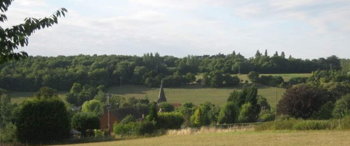 A rural landscape with a church, rolling hills, and a field.