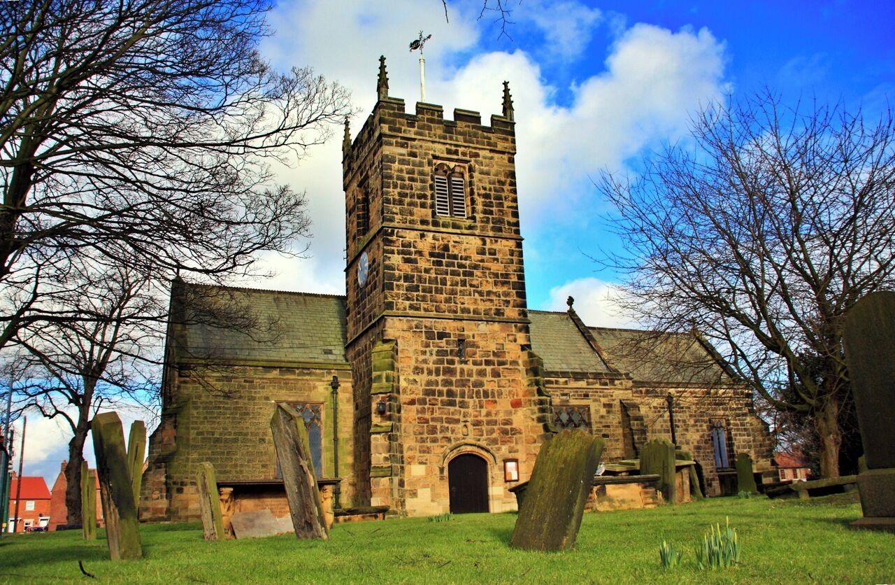 A historic stone church with a tall tower, surrounded by a cemetery with headstones.