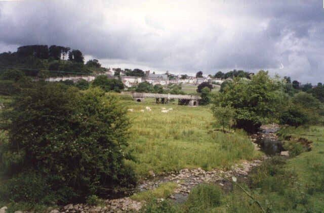 A rural landscape with a stone bridge, a stream, and lush greenery.