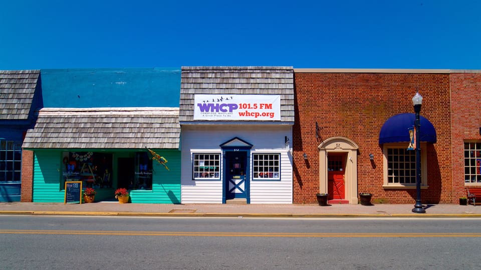 Una calle con una fachada azul, un edificio blanco con un letrero para WHCP 101.5 FM, y un edificio de ladrillo rojo con un toldo azul.