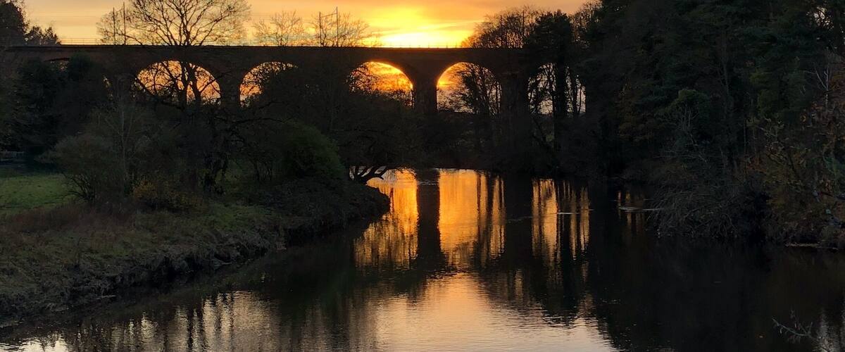 A stone bridge over a calm river at sunset.