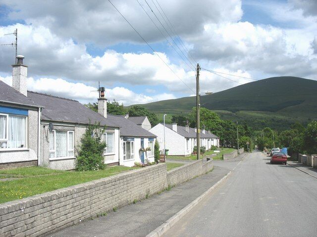 A residential street with houses, a brick wall, and a hill in the background.