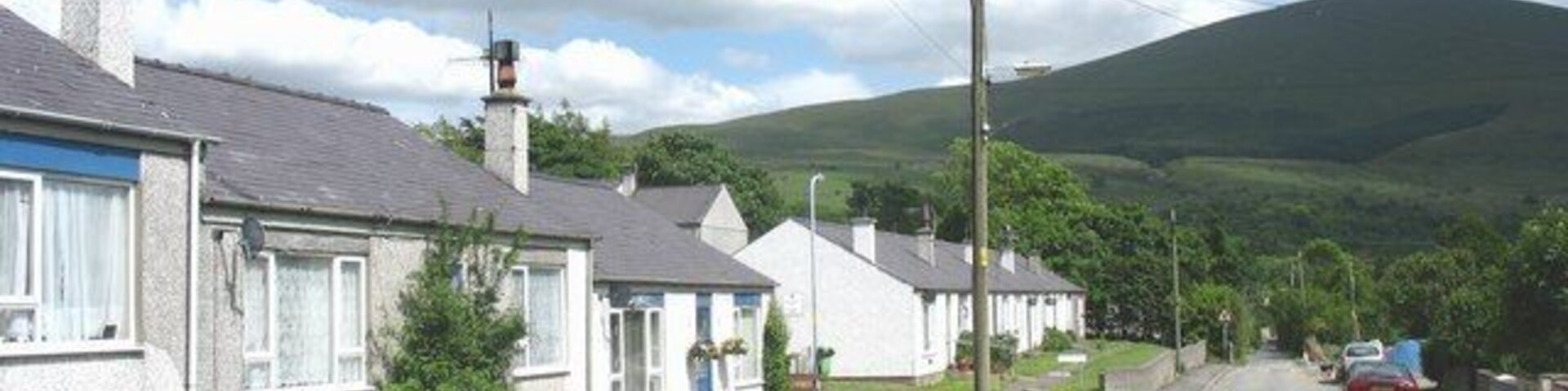 A residential street with houses, a brick wall, and a hill in the background.