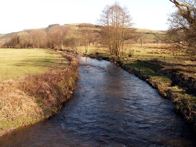 A narrow river flowing through a rural landscape with grassy fields and trees.
