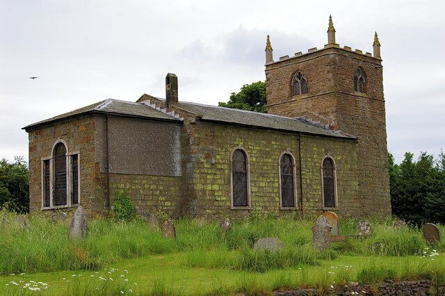 An old church with a bell tower and a stone building surrounded by grass and gravestones.