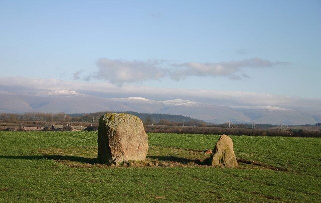 A stone monument in a grassy field with a mountainous background.