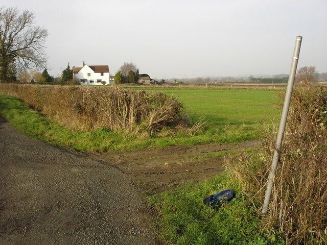 A rural road with a white house in the background, a metal post, and a blue object on the ground.