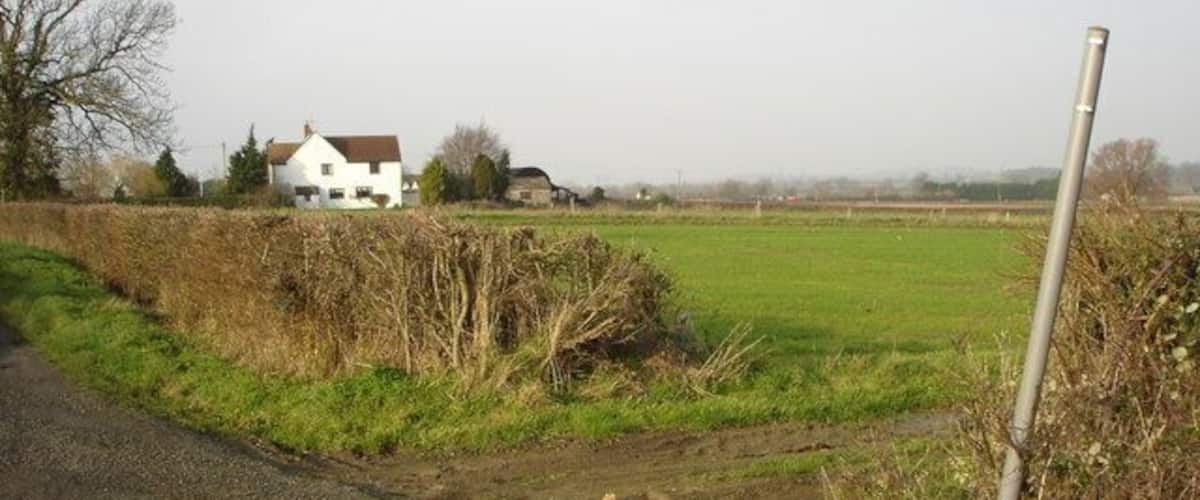 A rural road with a white house in the background, a metal post, and a blue object on the ground.