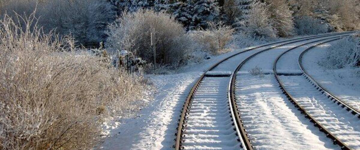 A snow-covered railway track curving through a forest.