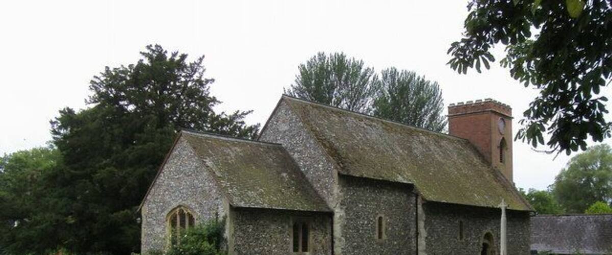 A stone church with a bell tower, surrounded by a cemetery and lush greenery.