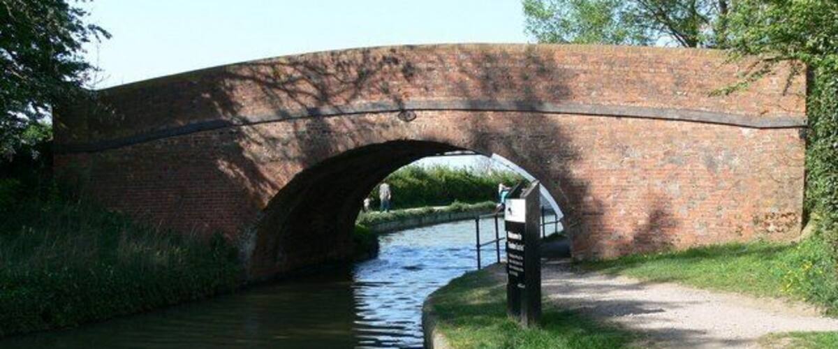 A brick bridge over a narrow canal with a path beside it.