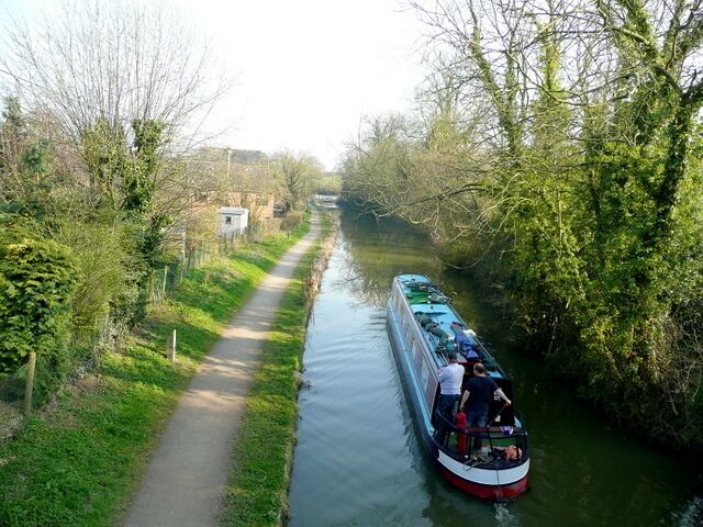 A narrow canal with a narrowboat and a path alongside it.