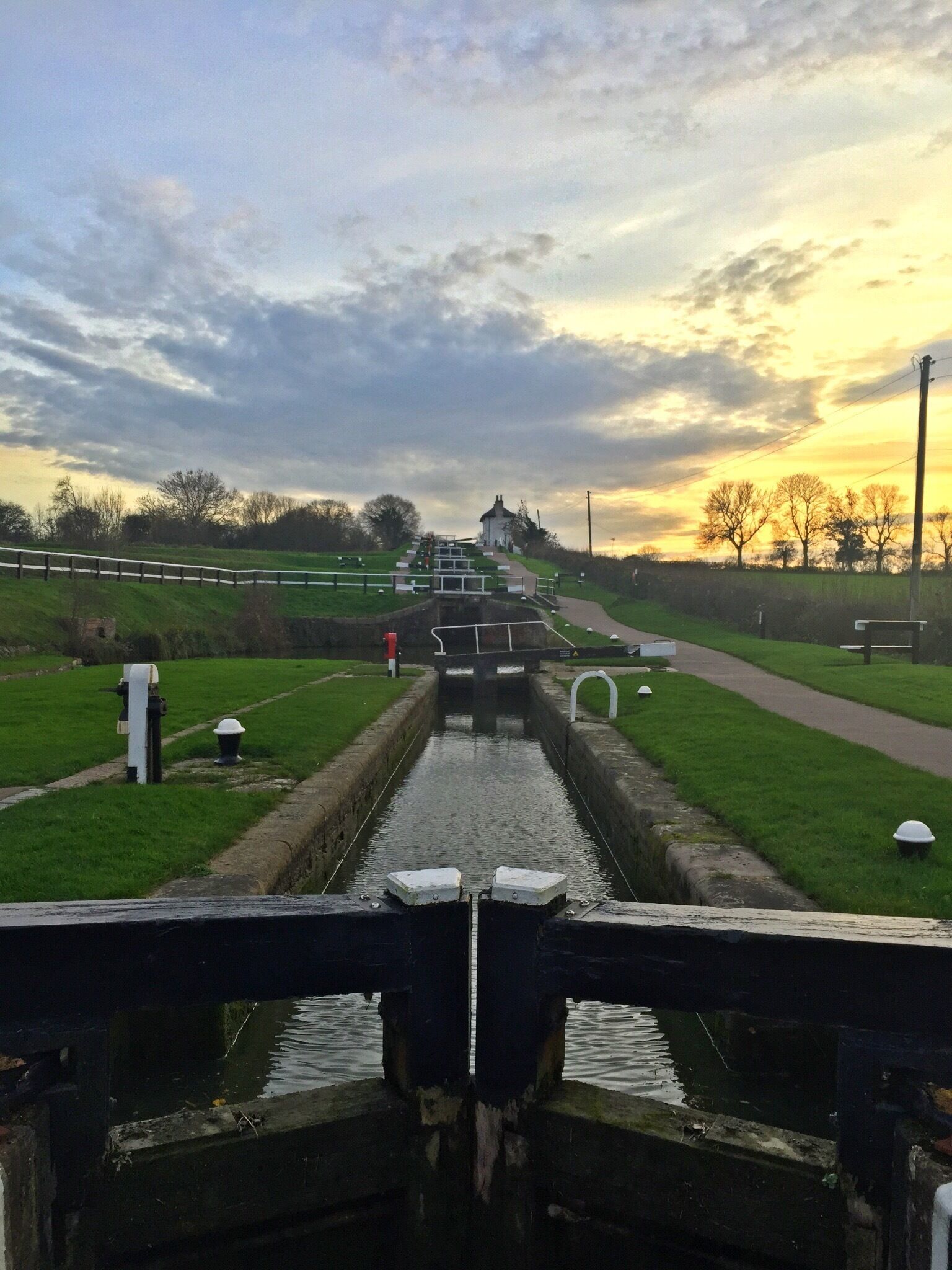 A canal with a lock system, surrounded by grassy areas and a small building in the distance.