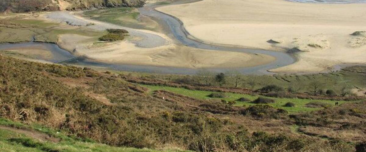 Paisaje costero con una playa arenosa, colinas ondulantes y un río serpenteante.