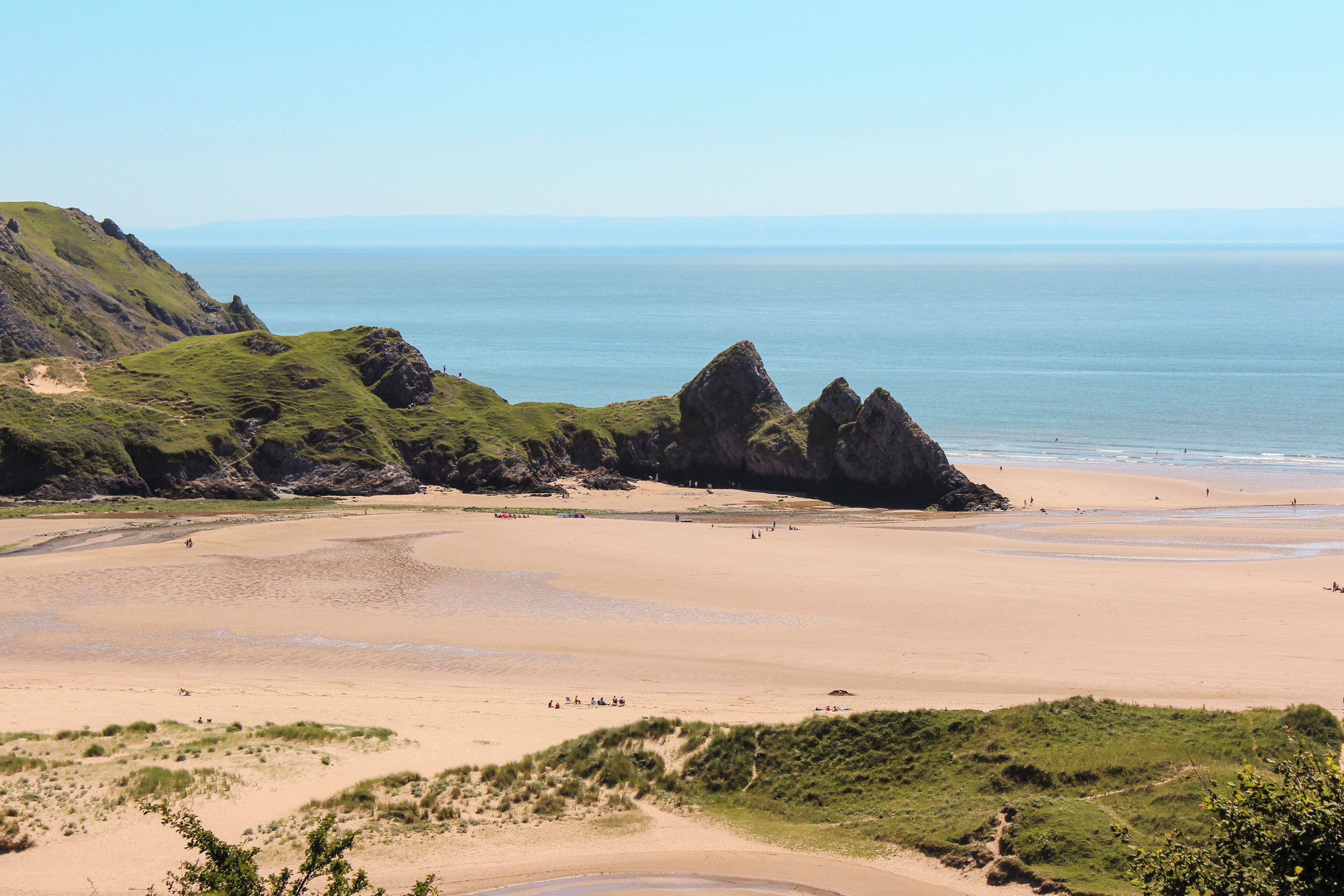 A coastal landscape with a sandy beach, grassy hills, and rocky formations.