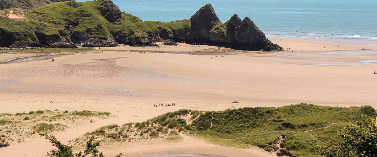 A coastal landscape with a sandy beach, grassy hills, and rocky formations.