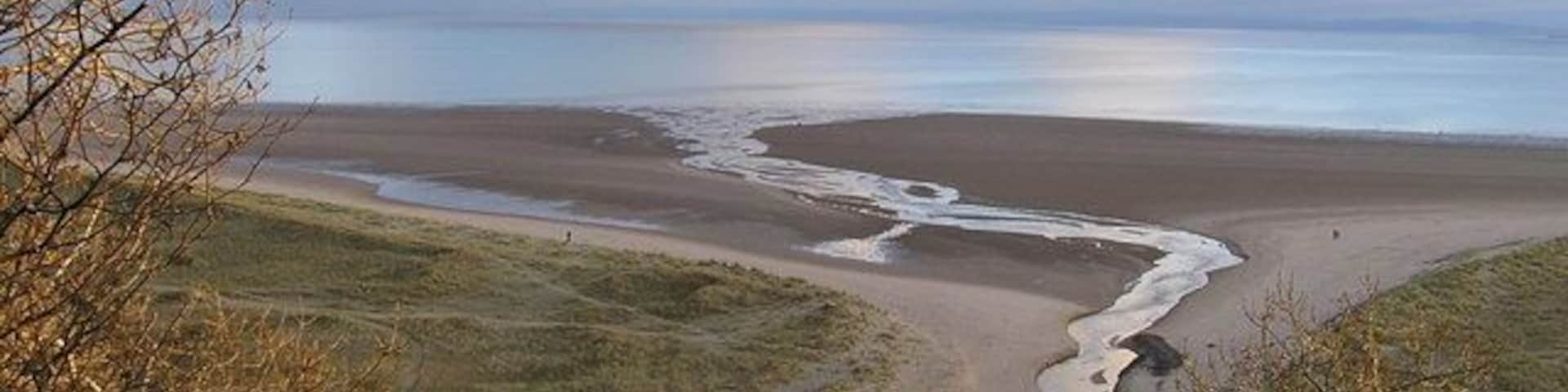 Un paisaje costero con una playa arenosa, un estrecho canal de agua y terreno cubierto de hierba.