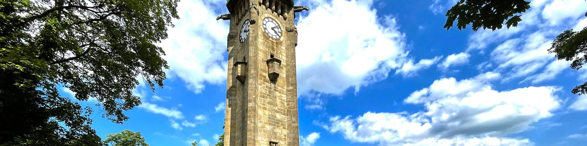 A historic clock tower, a street with cars, and a clear blue sky with clouds.