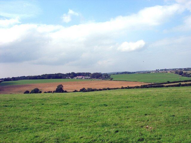 A rural landscape with fields, a distant village, and a cloudy sky.