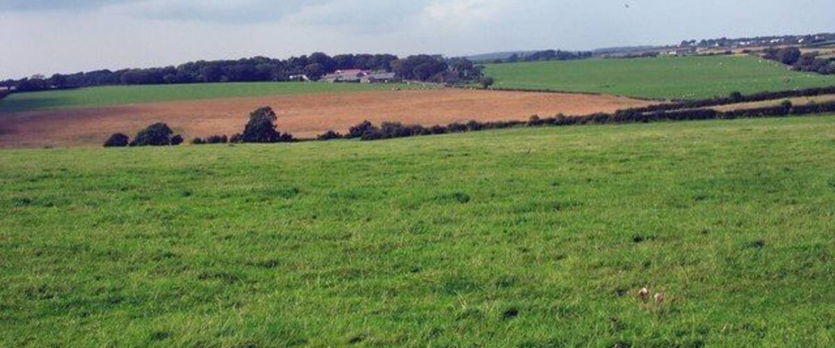 A rural landscape with fields, a distant village, and a cloudy sky.