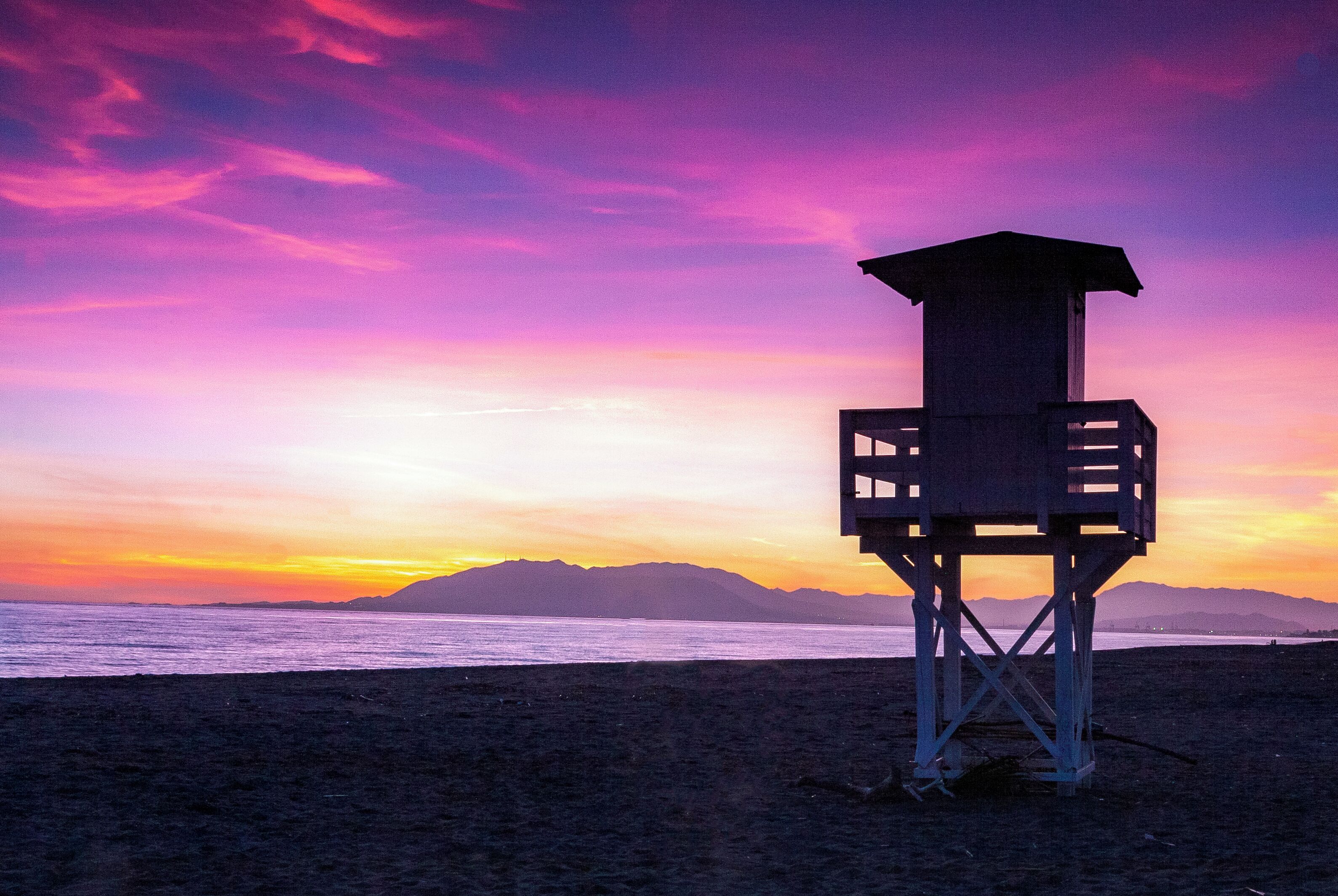 A lifeguard tower on a beach with a sunset sky.