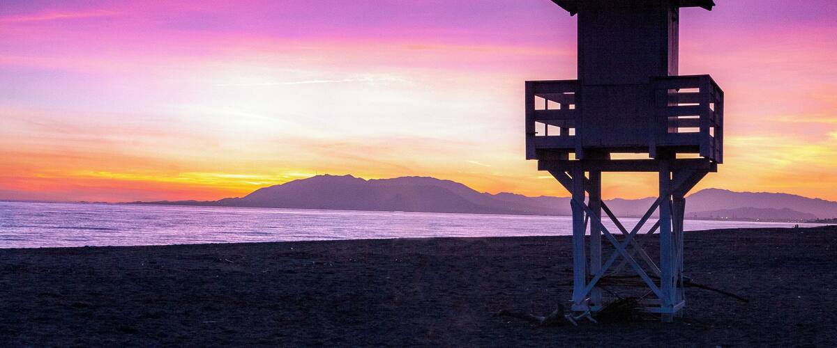 A lifeguard tower on a beach with a sunset sky.