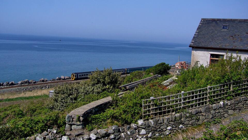 A coastal landscape with a train track, a stone wall, and a building near the sea.