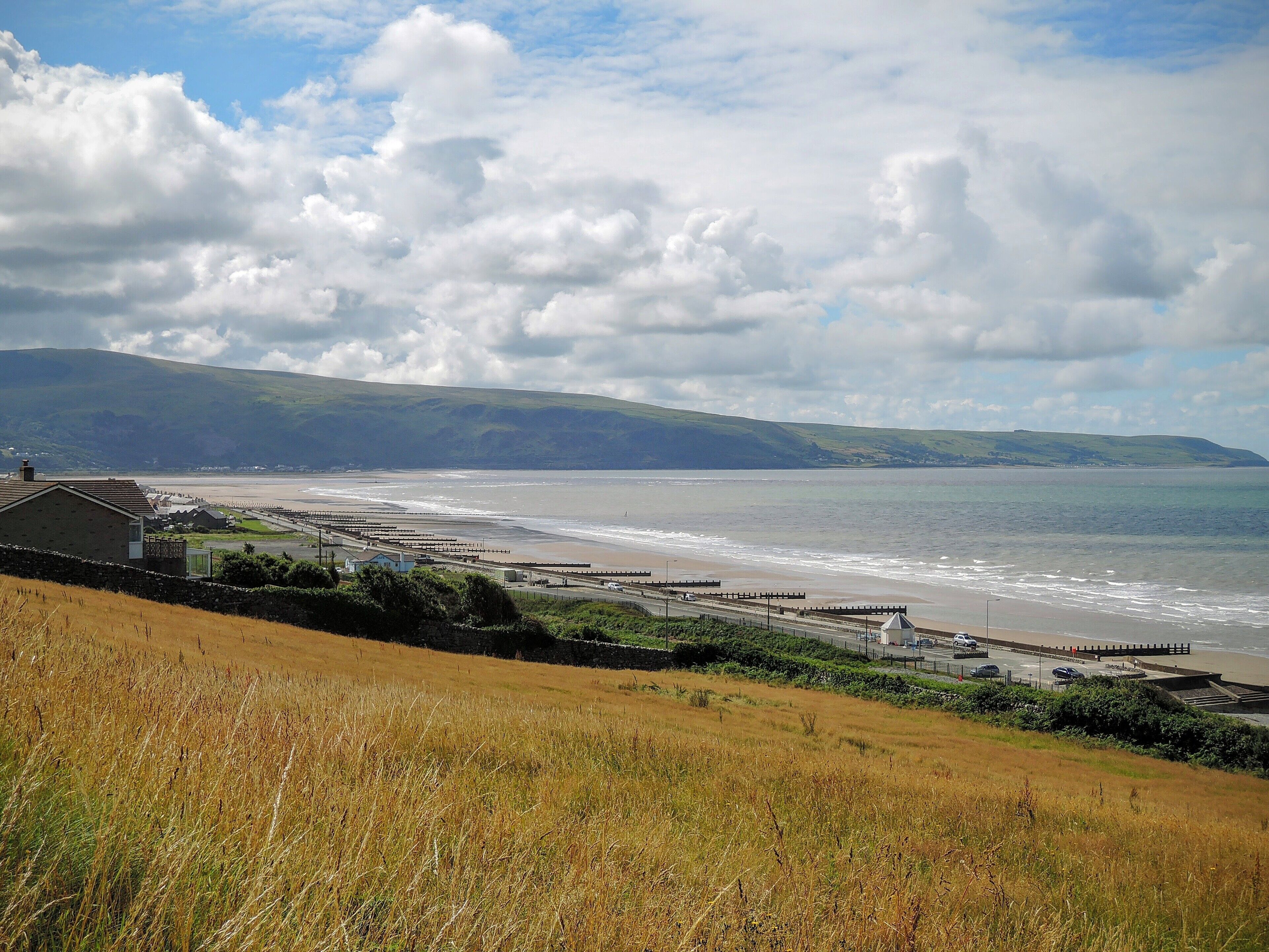 A coastal landscape with a beach, grassy fields, and a hilly backdrop.