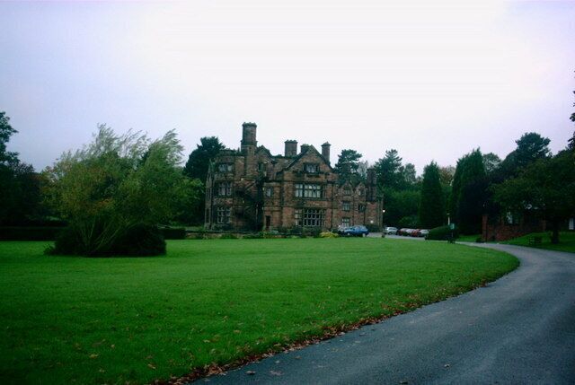 A large, historic stone building with a green lawn and a curved road in the foreground.