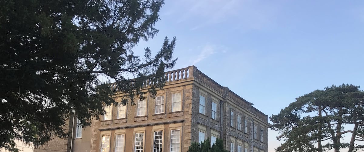 A large, historic building with a symmetrical facade, surrounded by well-maintained gardens and tall trees.