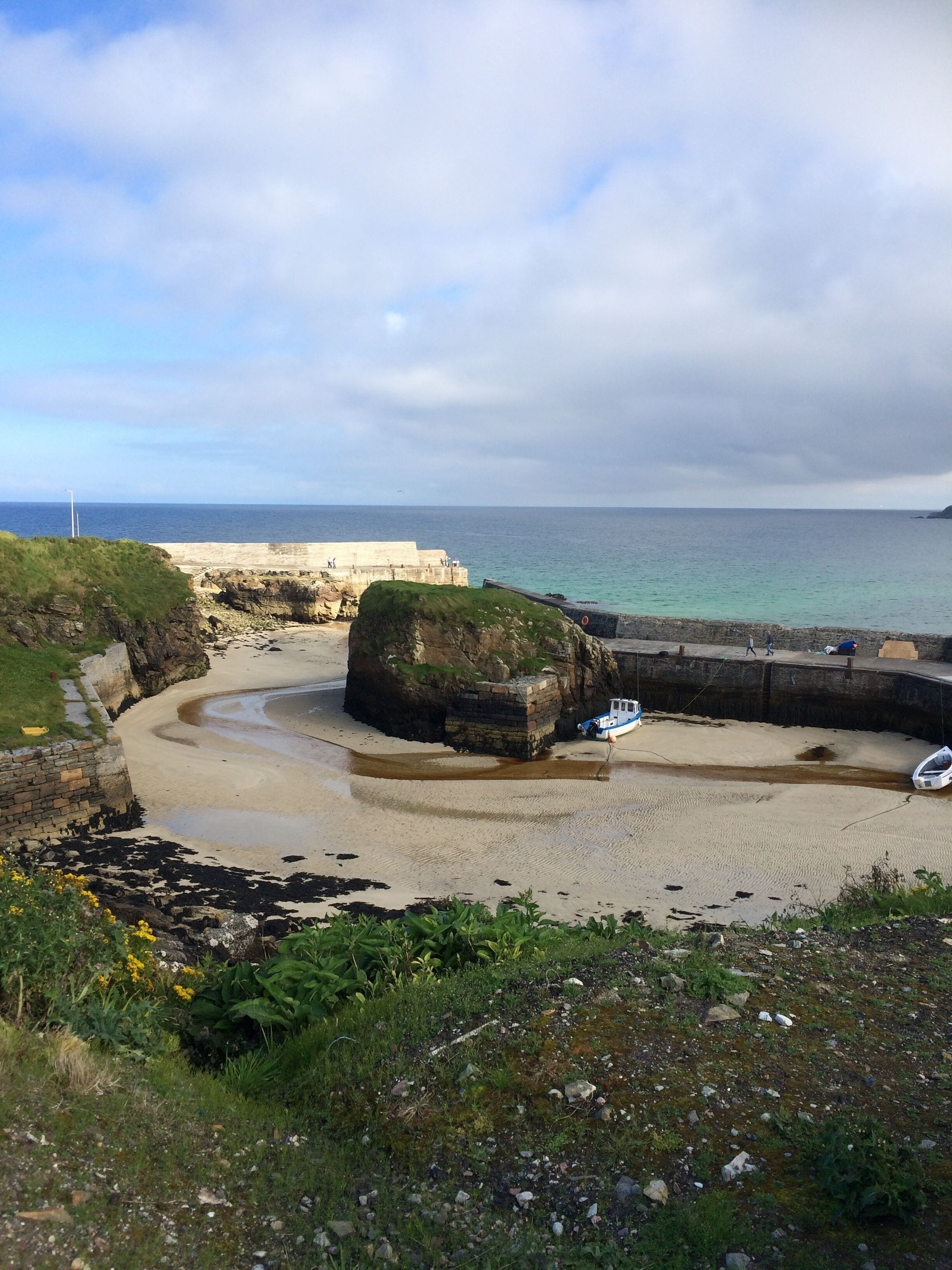 A coastal landscape with a large rock formation, a sandy beach, and a calm sea.