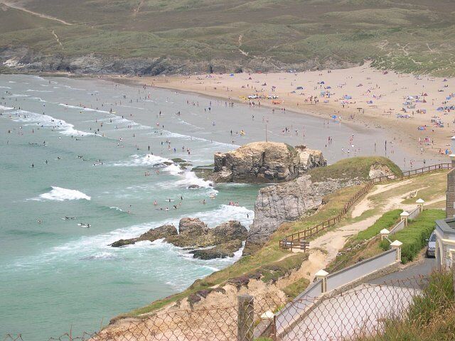 A coastal beach with rocky outcrops, a sandy shore, and a fence overlooking the area.
