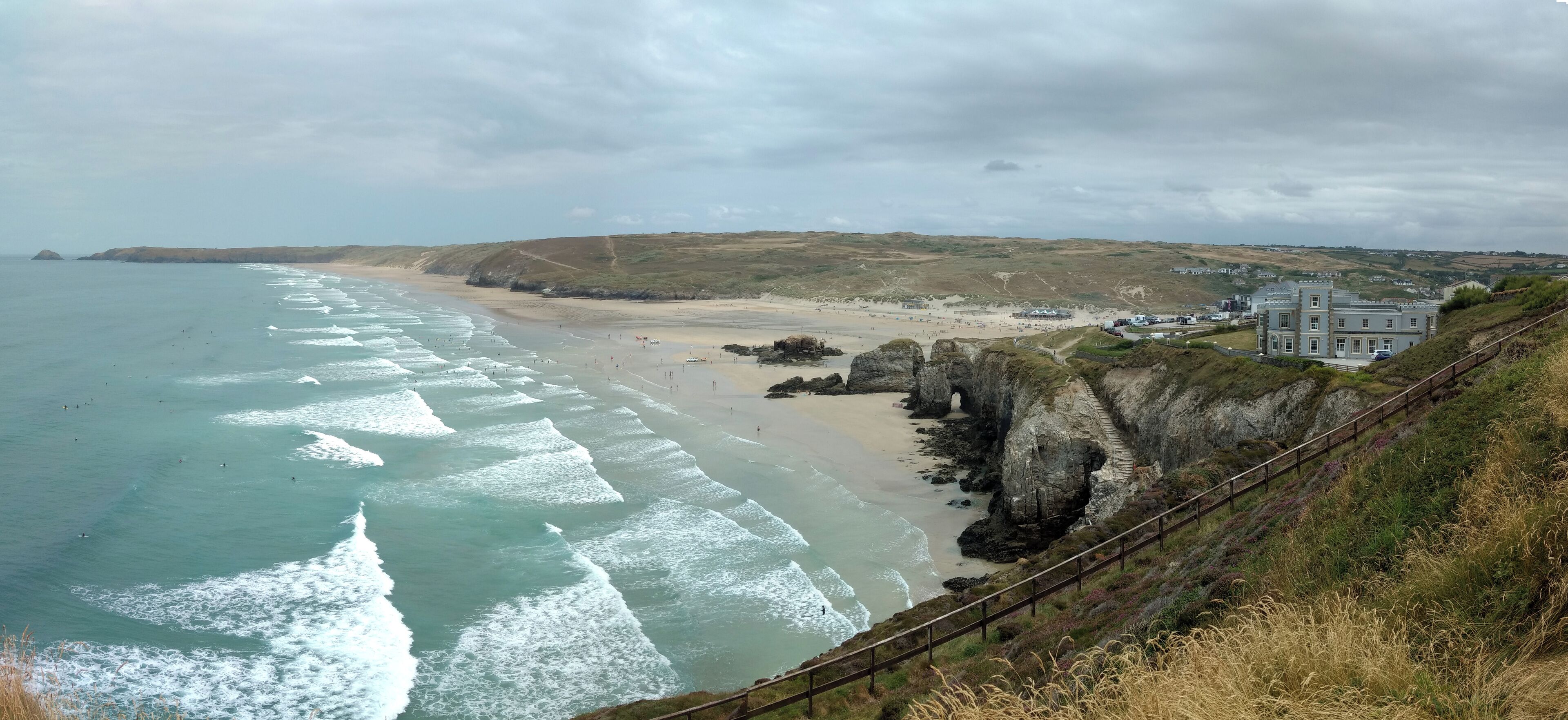 A coastal landscape with a beach, waves, cliffs, and a building.