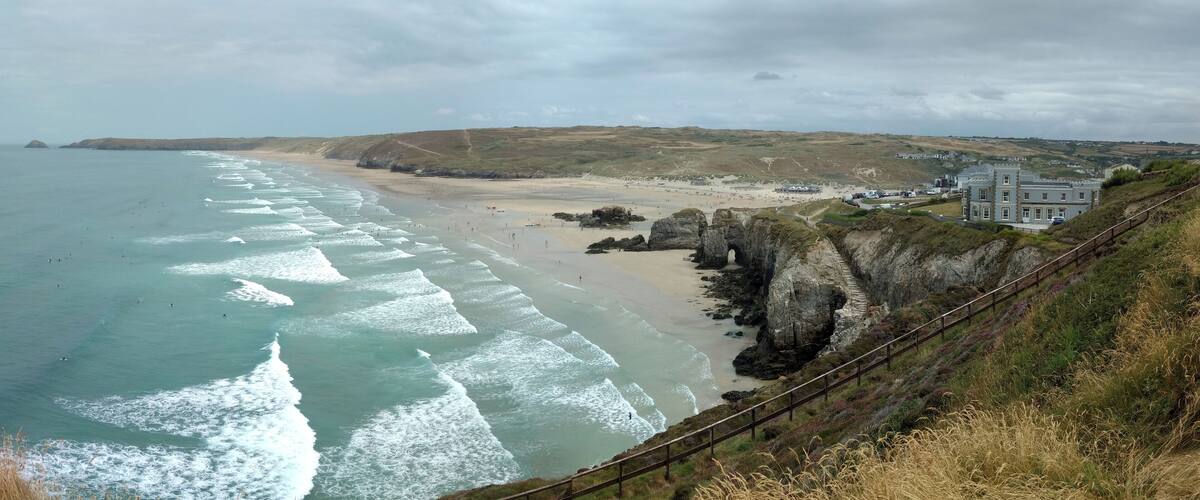 A coastal landscape with a beach, waves, cliffs, and a building.