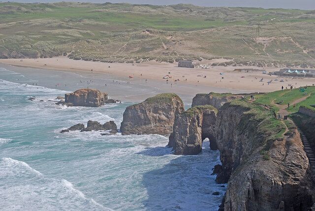 A coastal landscape with rocky cliffs, a beach, and a clear sky.