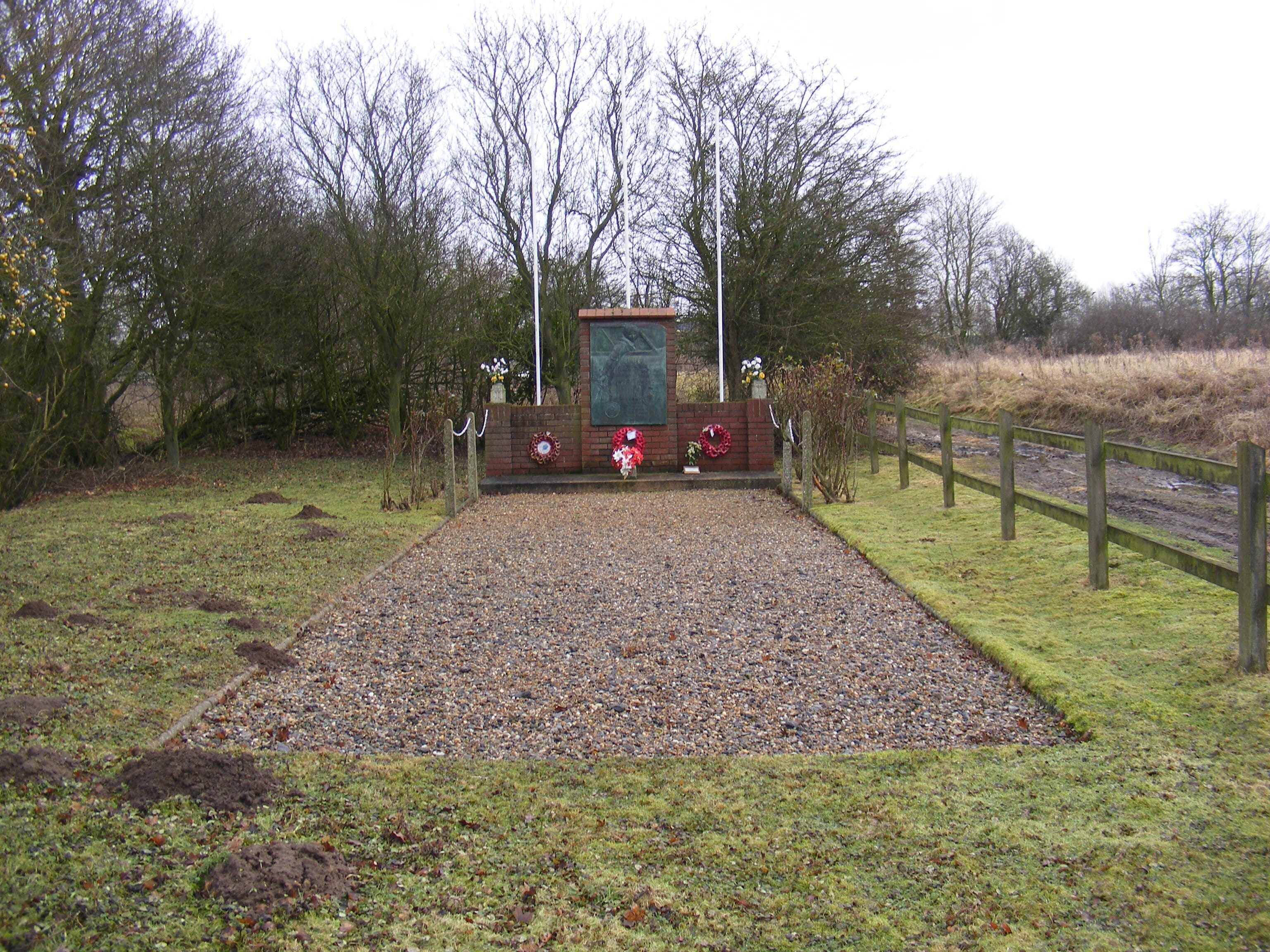 A memorial with a brick wall, wreaths, and a gravel path.