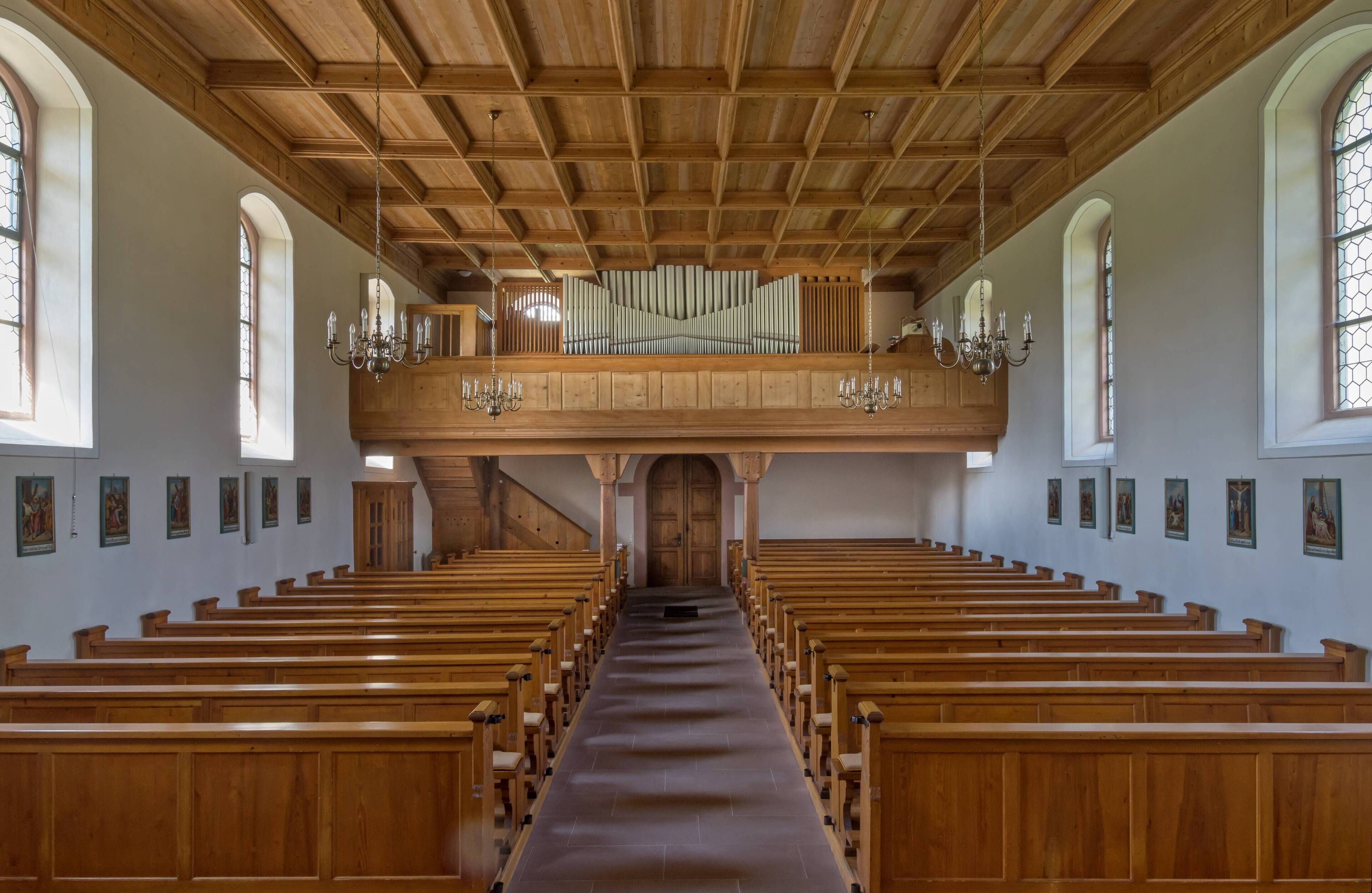 A church interior with wooden pews, a wooden organ loft, and arched windows.