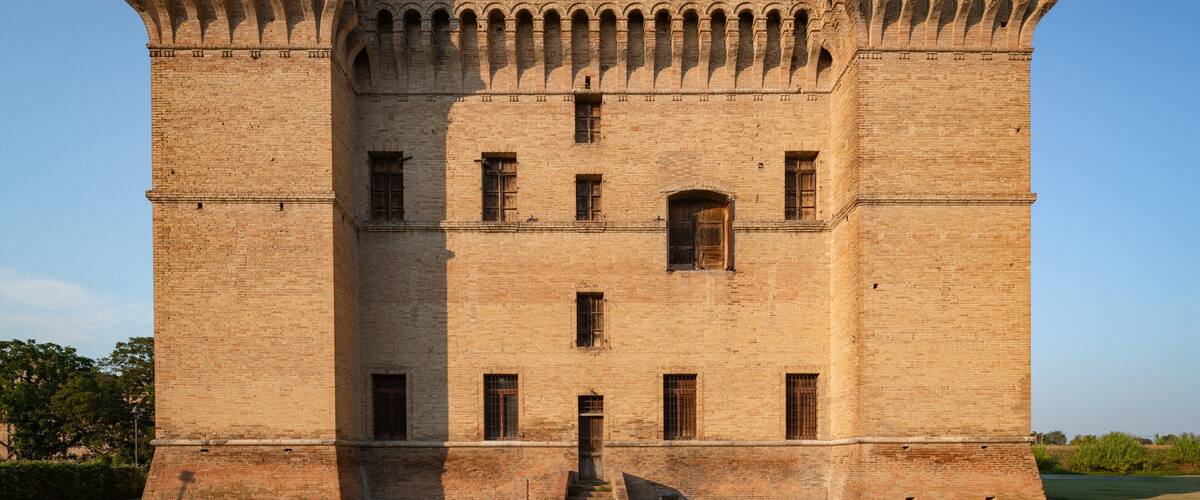 A large, historic brick castle with multiple arched windows and a central entrance.