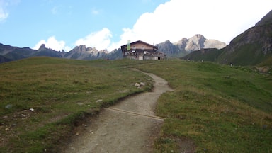 A mountain path leading to a chalet with a mountain backdrop.