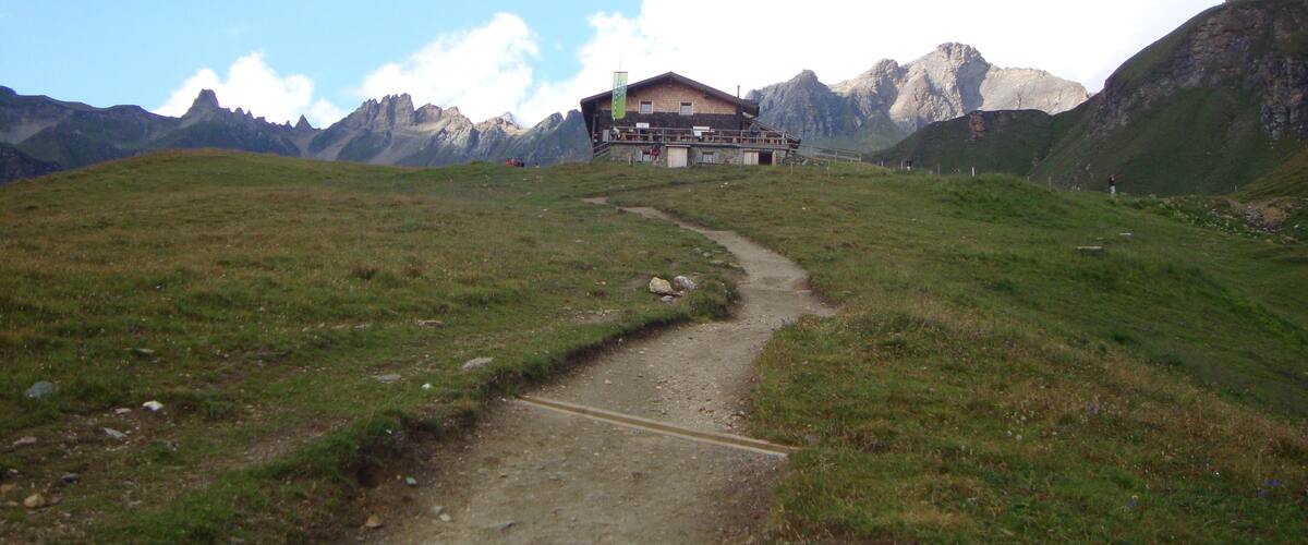 A mountain path leading to a chalet with a mountain backdrop.