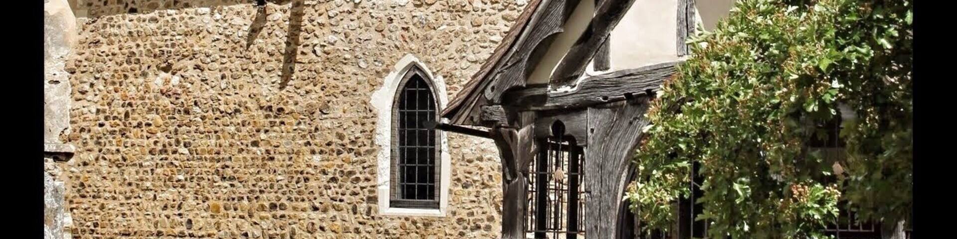 A church with a stone facade, a wooden tower, and a black gate.