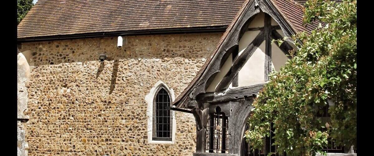 A church with a stone facade, a wooden tower, and a black gate.