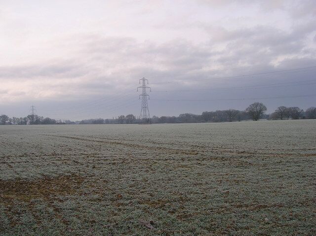 A frosty field with a power line tower in the distance.