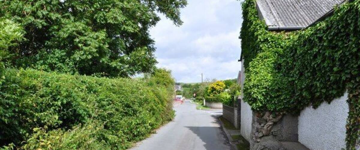 A narrow rural road flanked by lush greenery and a stone wall.
