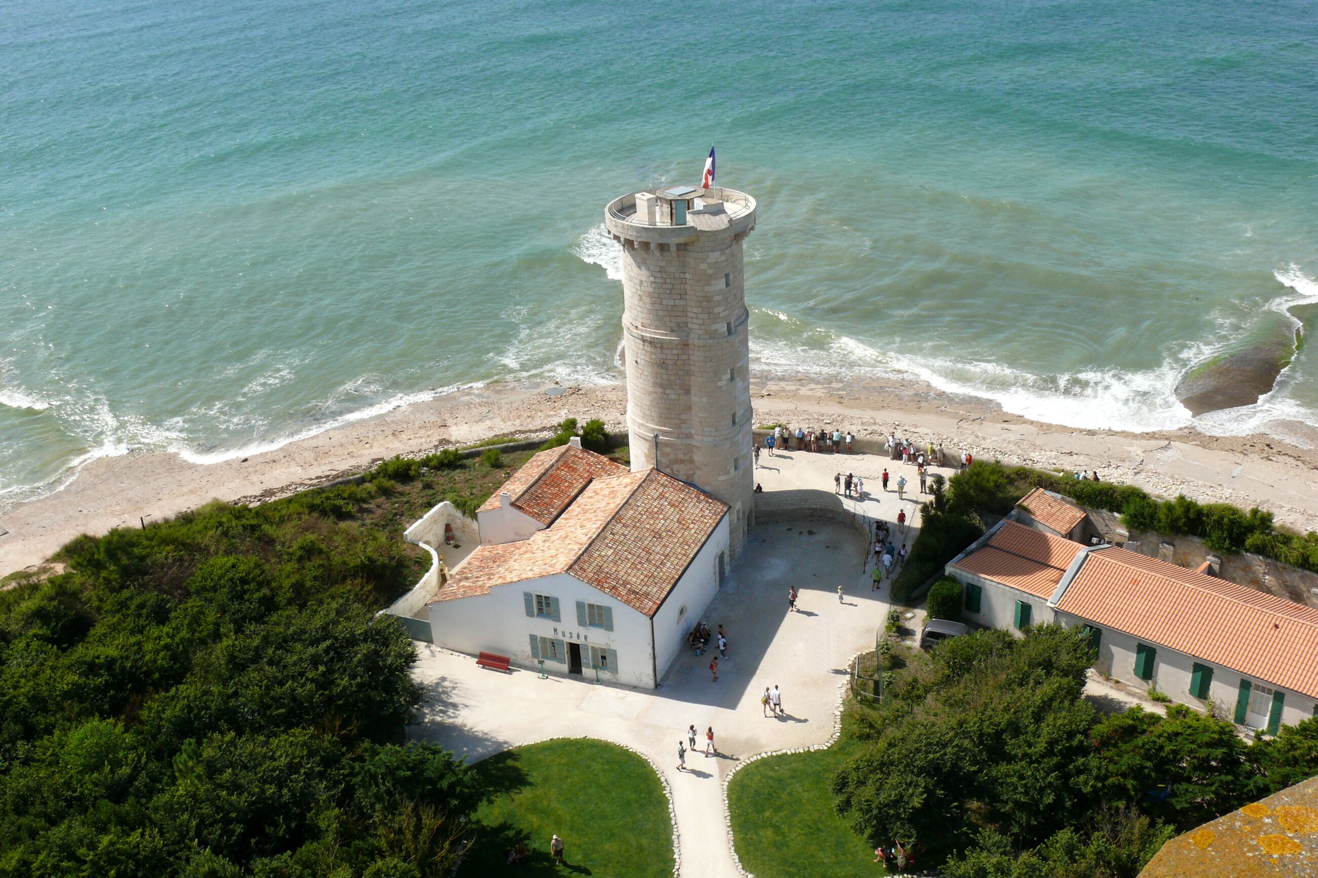 A coastal tower with a flag, a beach, and a white building with a red roof.