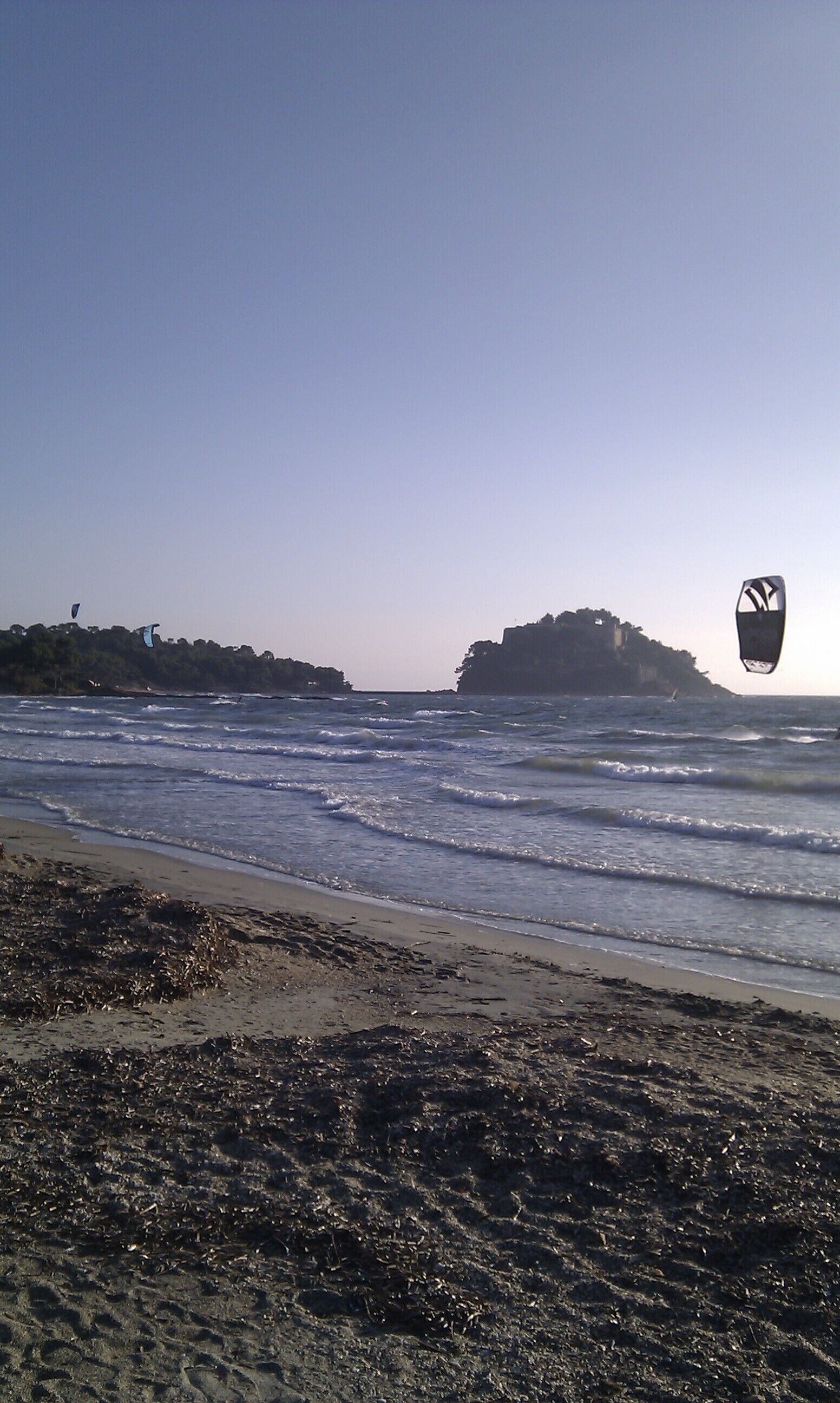 A beach with waves, a kite surfer, and rocky cliffs in the background.