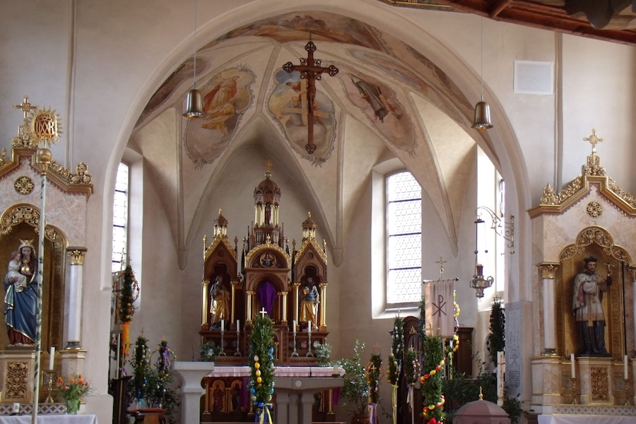 A church interior with ornate altars, statues, and a vaulted ceiling.