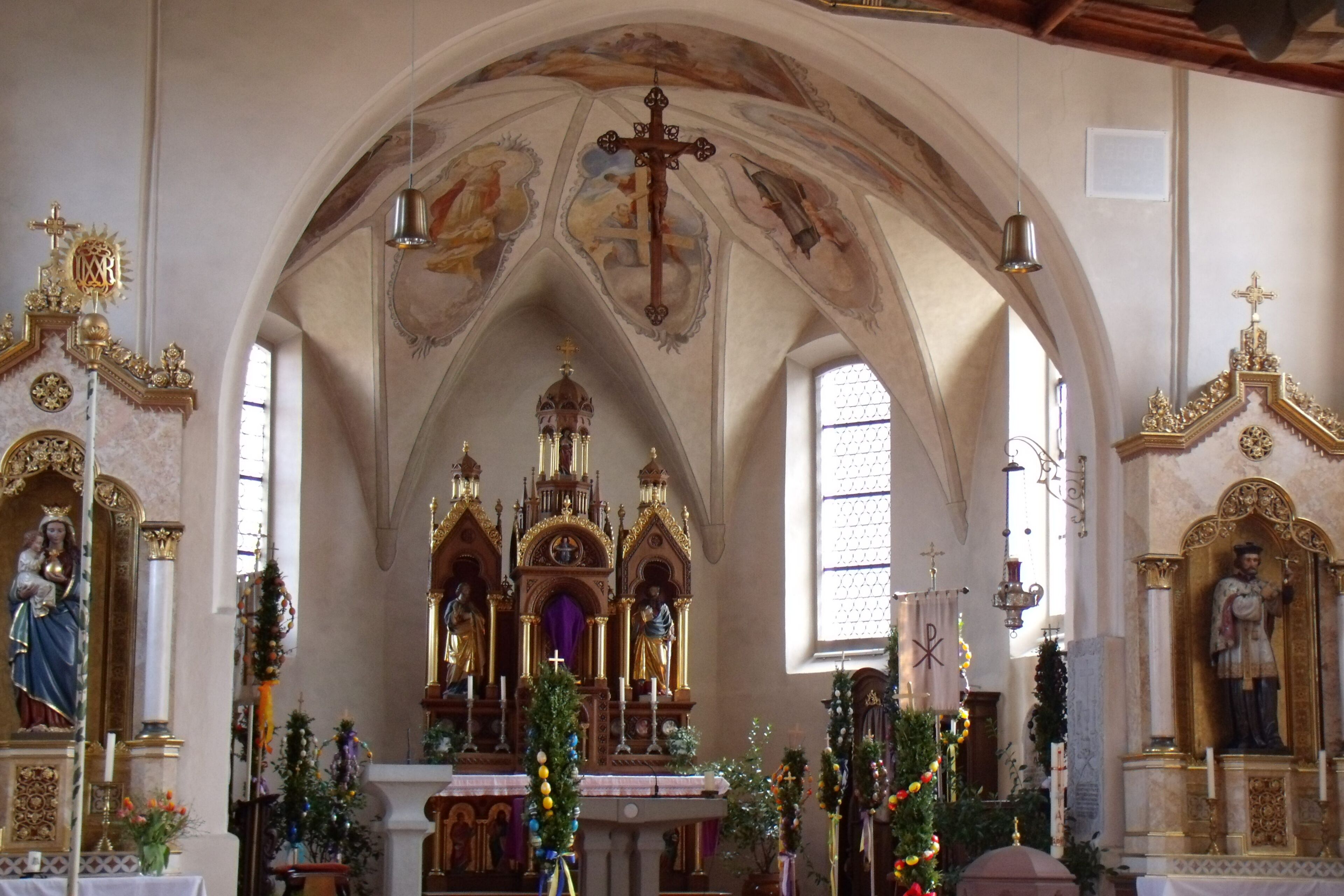 A church interior with ornate altars, statues, and a vaulted ceiling.