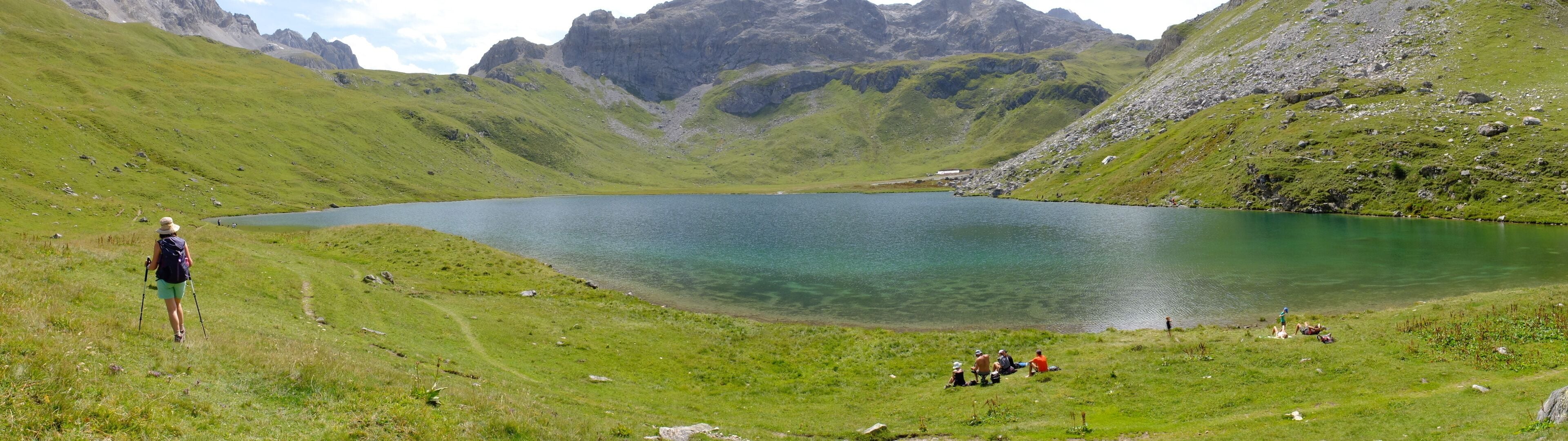 A lake surrounded by green hills and rocky mountains.