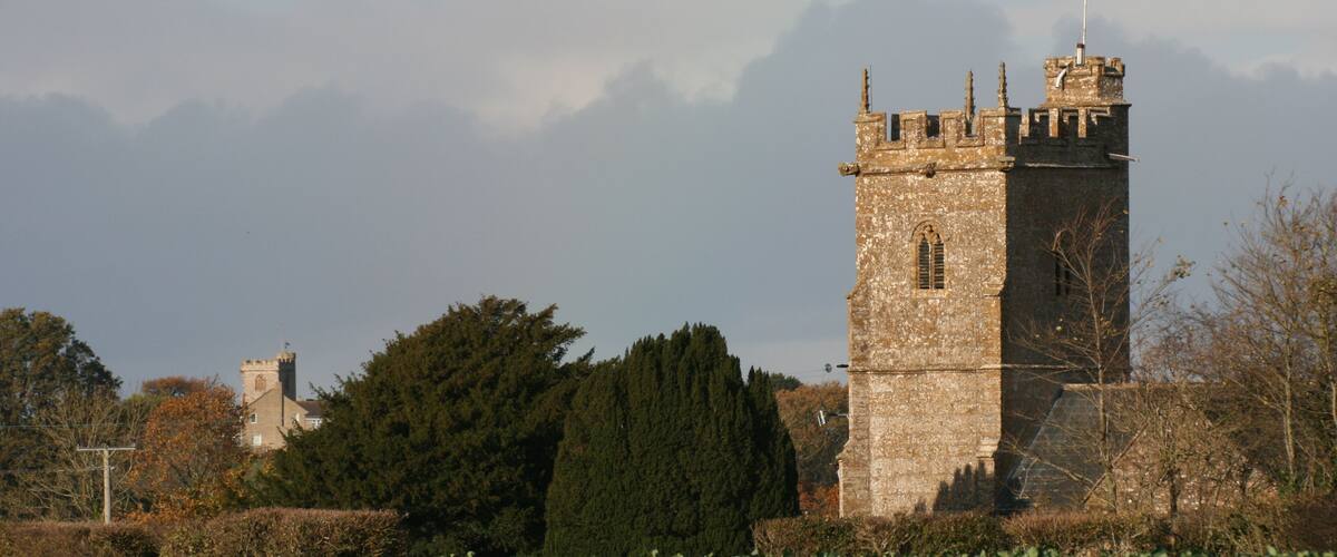 A stone tower with a flag atop, surrounded by trees and a field.